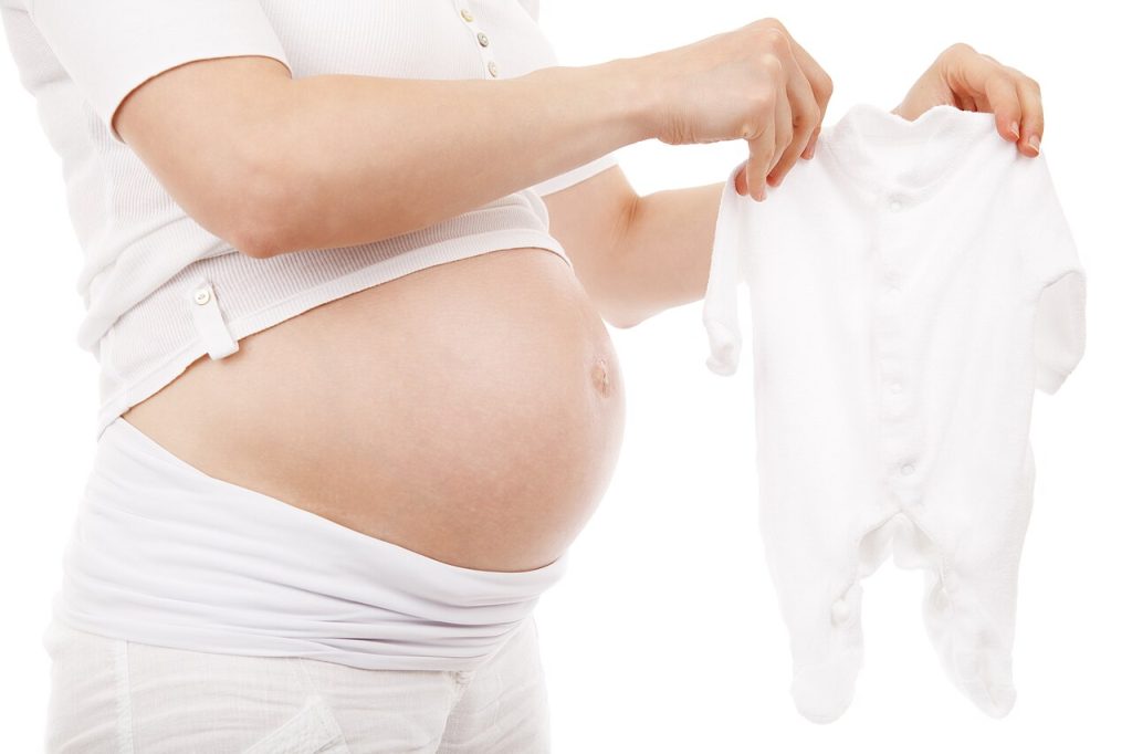 Pregnant person holding a white baby sleeper